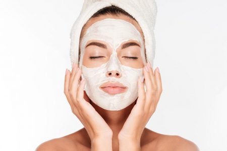 Beautiful woman with eyes closed and white clay facial mask on face isolated on white background