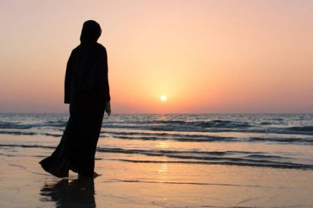 Woman in hijab standing on the beach looking at horizon