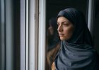 Young Muslim woman is looking worried through the window.