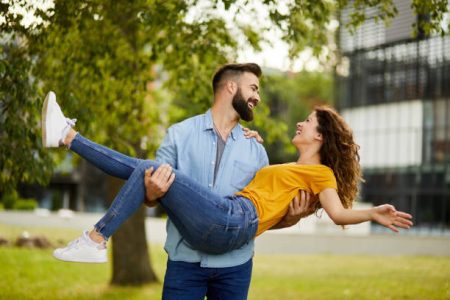 Man carrying his girlfriend in arms, spinning her around in the park